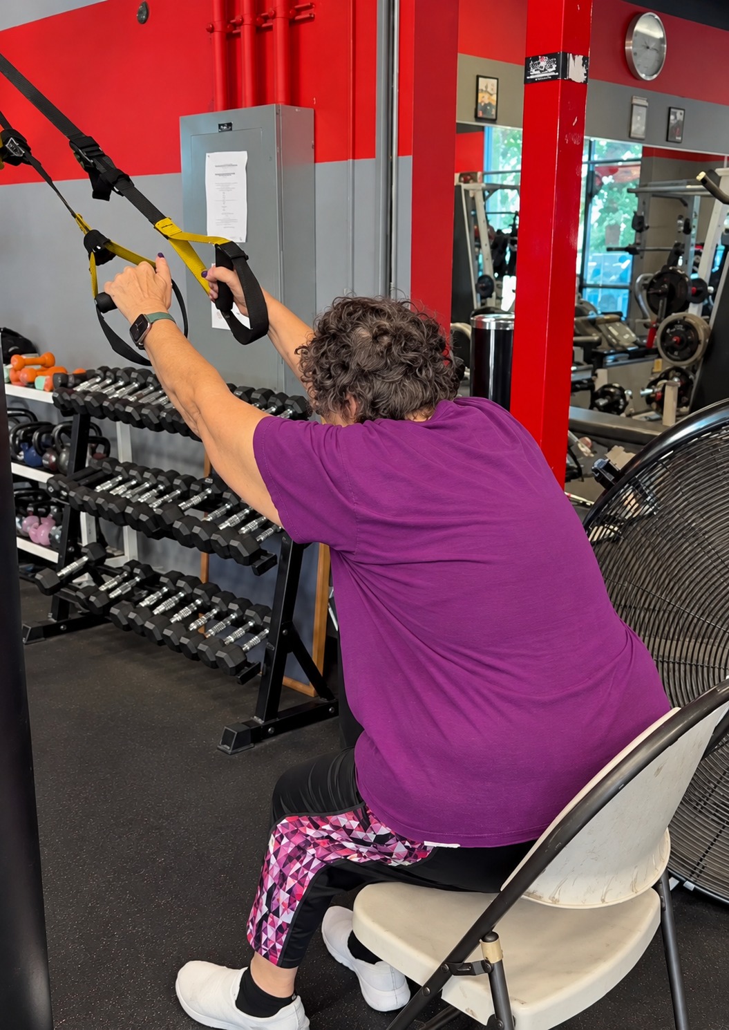 Seated senior member holding suspension training straps during an adaptive exercise